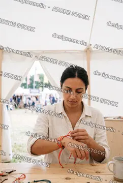 Focused Young Artisan Woman Putting On A Handmade Braided Bracelet Inside A Craft Tent At An Outdoor Summer Festival Market