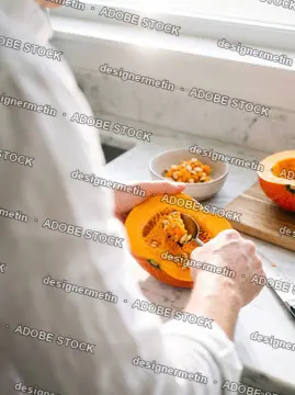 Close-Up Of A Person Scooping Out Pumpkin Seeds With A Spoon On A Bright Marble Kitchen Counter