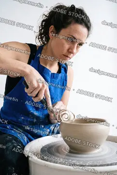 Focused Female Potter Carving And Trimming A Ceramic Clay Bowl On A Spinning Pottery Wheel In A Creative Art Studio