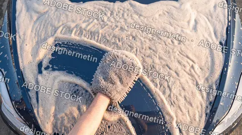 Person Washing A Car Hood Covered With Thick Soap Foam Using A Microfiber Wash Mitt During Auto Detailing