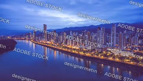 City Skyline At Dusk Along A River, Illuminated Skyscrapers And Reflections Under Blue Sky